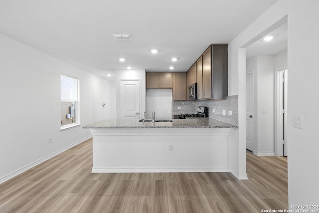 kitchen featuring sink, decorative backsplash, light hardwood / wood-style floors, kitchen peninsula, and light stone countertops