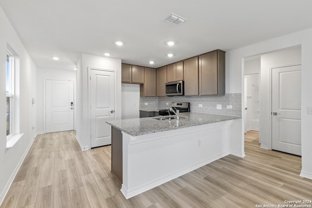 kitchen featuring sink, light stone counters, appliances with stainless steel finishes, kitchen peninsula, and decorative backsplash