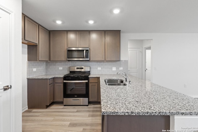 kitchen with stainless steel appliances, light stone countertops, sink, and light hardwood / wood-style floors