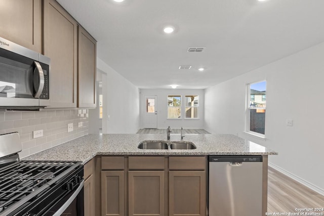 kitchen with sink, appliances with stainless steel finishes, backsplash, light stone countertops, and kitchen peninsula