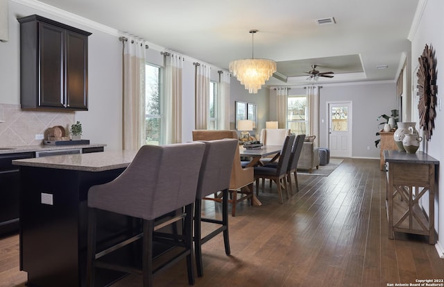 dining area with a raised ceiling, a healthy amount of sunlight, dark hardwood / wood-style floors, and ornamental molding