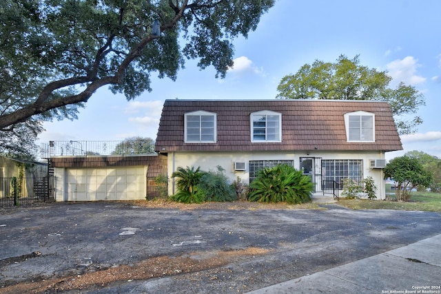 front of property featuring stucco siding, a wall mounted AC, mansard roof, aphalt driveway, and a garage