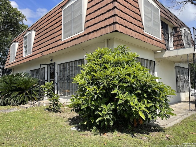 view of property exterior featuring a balcony, a tiled roof, mansard roof, and stucco siding