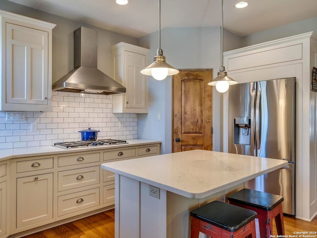 kitchen with a kitchen breakfast bar, a center island, hanging light fixtures, stainless steel appliances, and wall chimney range hood