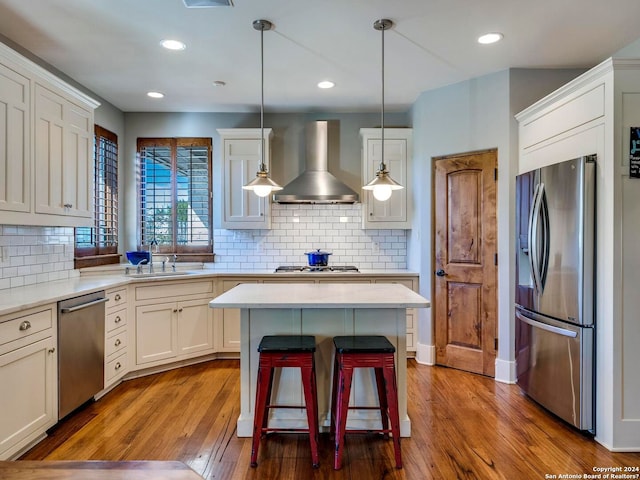 kitchen with pendant lighting, light countertops, appliances with stainless steel finishes, a sink, and wall chimney exhaust hood