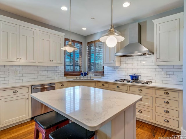 kitchen featuring wall chimney exhaust hood, a breakfast bar, stainless steel appliances, pendant lighting, and a sink