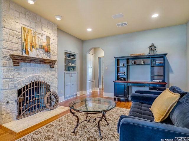 living room with arched walkways, a fireplace, visible vents, wood finished floors, and baseboards