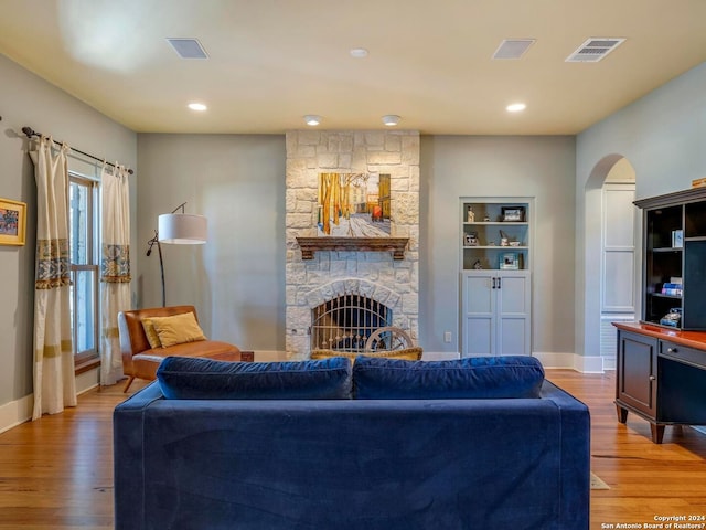 living room featuring visible vents, arched walkways, baseboards, light wood-style flooring, and a fireplace