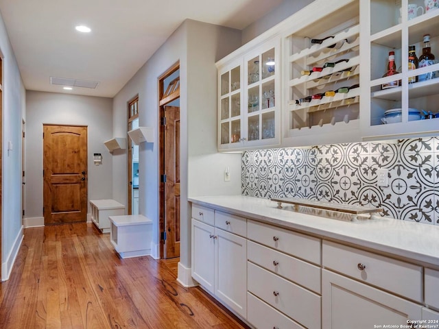 kitchen featuring tasteful backsplash, light countertops, glass insert cabinets, light wood-style floors, and white cabinetry