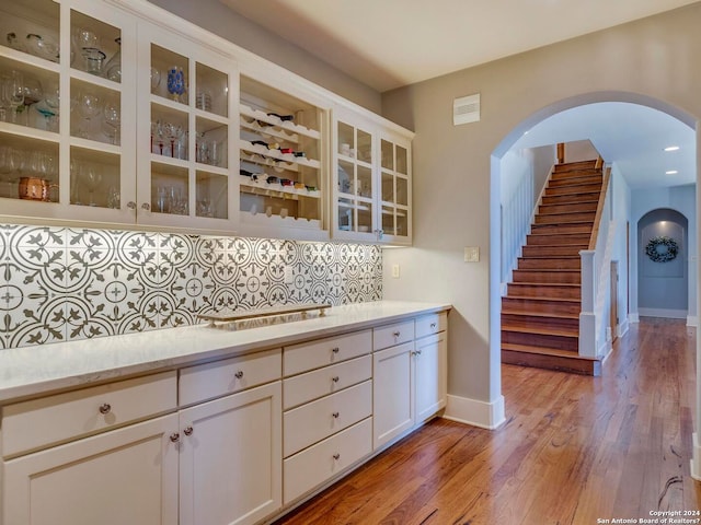 kitchen with arched walkways, white cabinets, light countertops, decorative backsplash, and glass insert cabinets