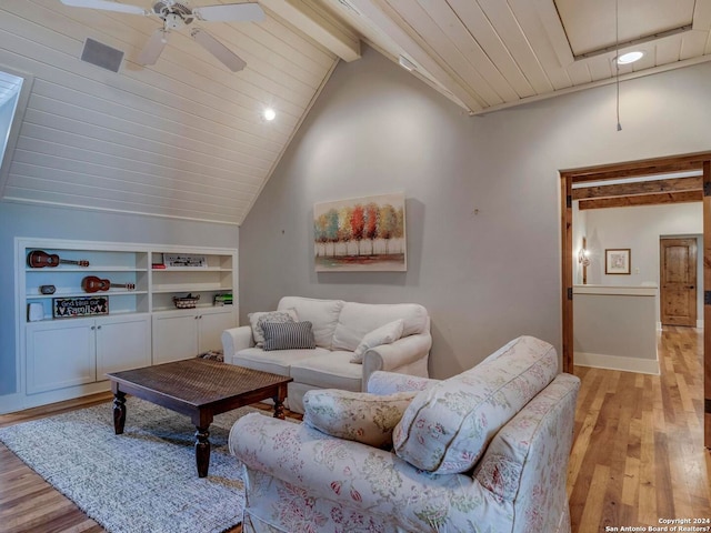 living area with built in shelves, light wood-style flooring, lofted ceiling with beams, attic access, and ceiling fan