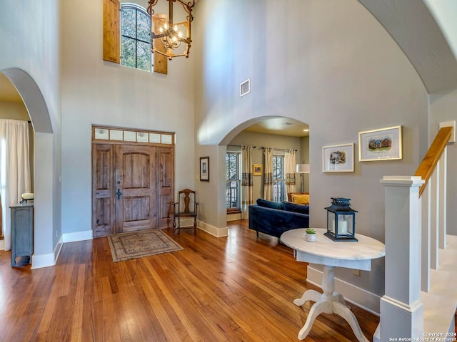 entrance foyer featuring arched walkways, visible vents, stairway, wood finished floors, and baseboards