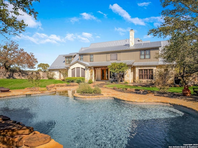 back of property featuring stone siding, a chimney, metal roof, and a standing seam roof