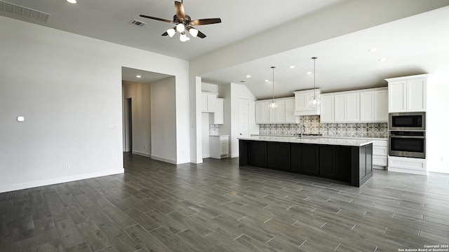 kitchen featuring built in microwave, oven, an island with sink, and white cabinets