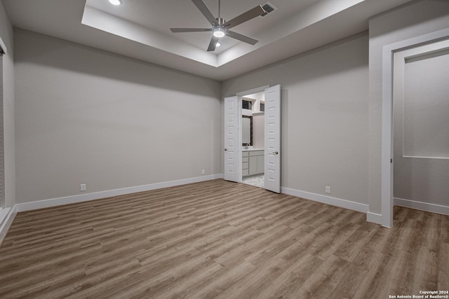 unfurnished bedroom featuring ensuite bath, a raised ceiling, ceiling fan, and light wood-type flooring