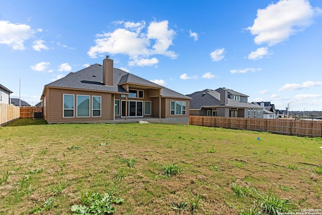 rear view of property featuring a yard, a chimney, and a fenced backyard