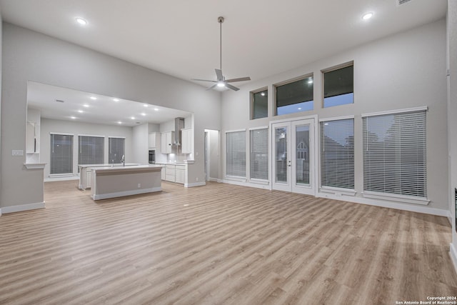 unfurnished living room featuring light wood-type flooring, baseboards, a towering ceiling, and a ceiling fan