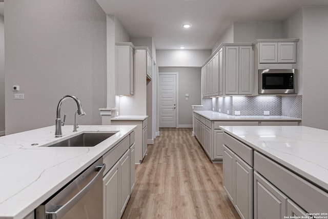 kitchen with sink, light hardwood / wood-style flooring, appliances with stainless steel finishes, backsplash, and light stone counters