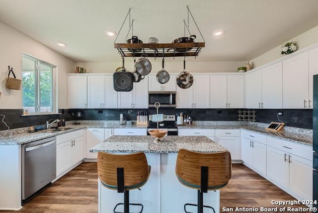 kitchen with appliances with stainless steel finishes, a center island, light stone counters, white cabinets, and a kitchen bar