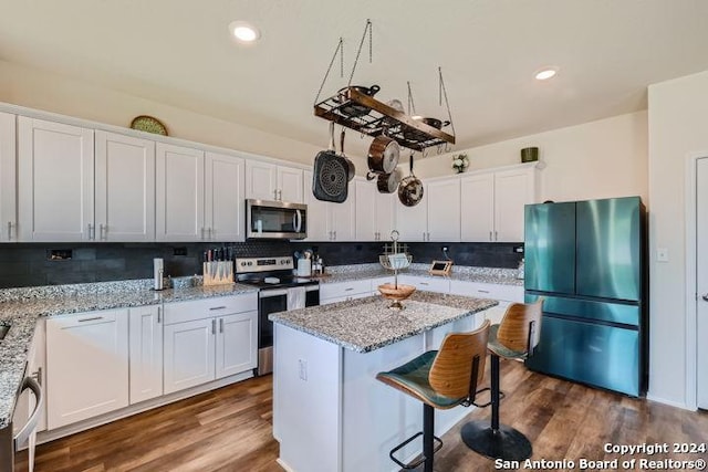 kitchen featuring a center island, stainless steel appliances, light stone countertops, and white cabinets