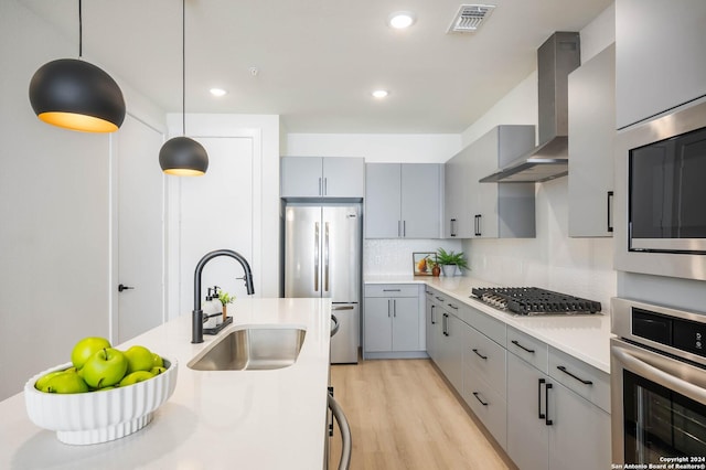 kitchen with sink, tasteful backsplash, decorative light fixtures, appliances with stainless steel finishes, and wall chimney range hood