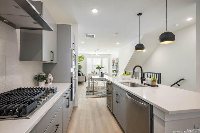 kitchen featuring appliances with stainless steel finishes, sink, hanging light fixtures, exhaust hood, and light hardwood / wood-style floors