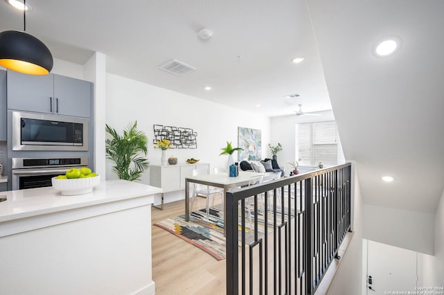 interior space featuring built in microwave, hanging light fixtures, ceiling fan, oven, and light hardwood / wood-style floors