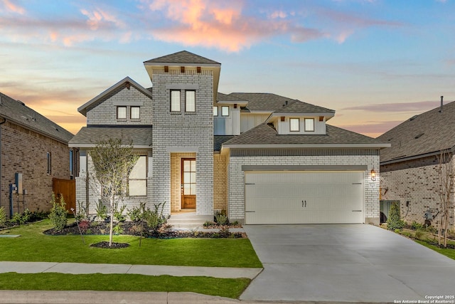 view of front of house featuring a shingled roof, concrete driveway, an attached garage, a yard, and brick siding