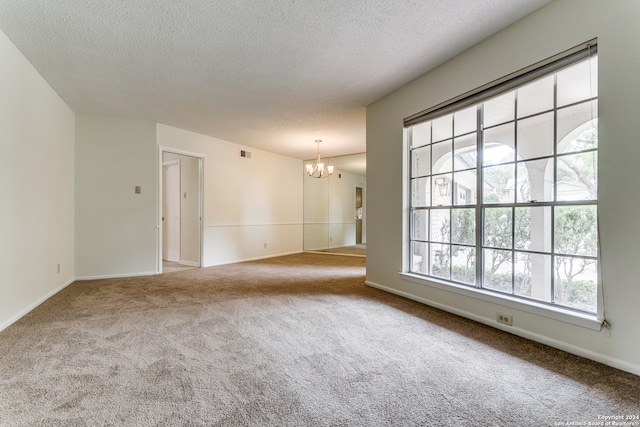 carpeted empty room featuring a chandelier and a textured ceiling