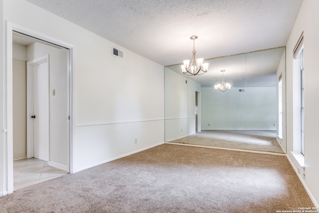 empty room with a chandelier, a textured ceiling, and light colored carpet