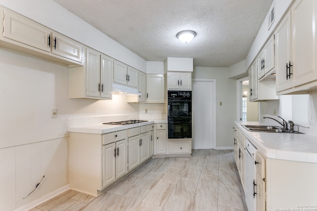 kitchen with white cabinetry, tile countertops, sink, double oven, and a textured ceiling