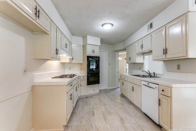 kitchen featuring white dishwasher, sink, black double oven, a textured ceiling, and tile countertops