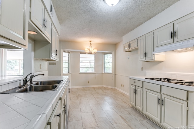 kitchen featuring white cabinetry, a chandelier, tile countertops, sink, and a textured ceiling