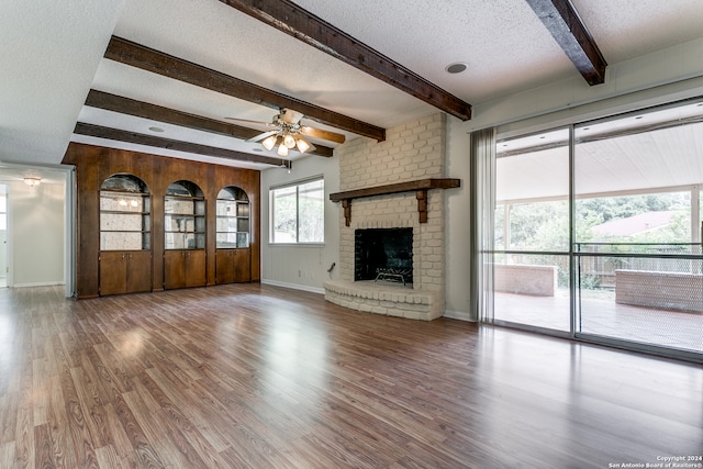 unfurnished living room featuring a fireplace, wood-type flooring, ceiling fan, beamed ceiling, and a textured ceiling