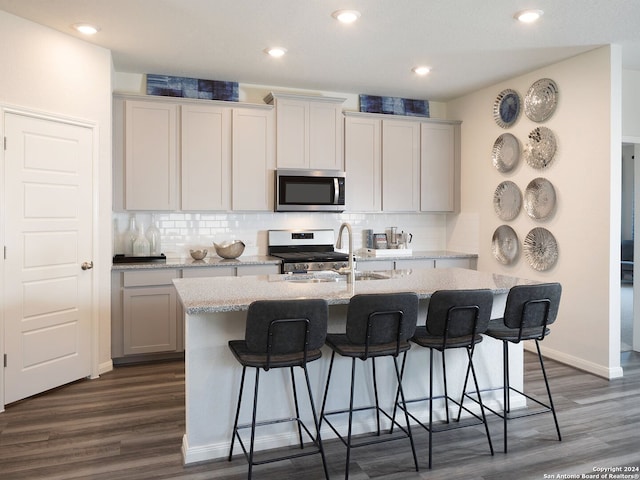 kitchen with appliances with stainless steel finishes, a breakfast bar area, a kitchen island with sink, dark wood-type flooring, and decorative backsplash