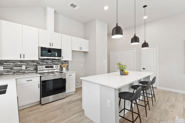 kitchen featuring appliances with stainless steel finishes, white cabinets, light wood-type flooring, a center island, and decorative light fixtures