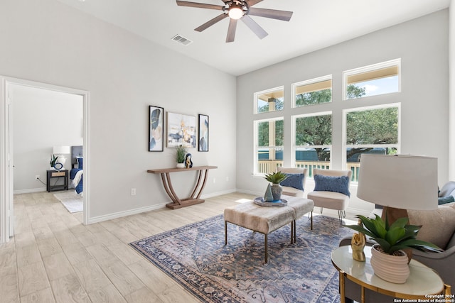 living room with ceiling fan, light hardwood / wood-style flooring, and a high ceiling