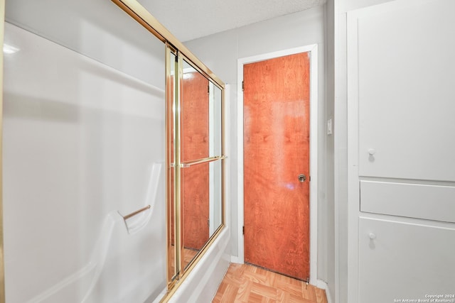 bathroom featuring enclosed tub / shower combo, parquet flooring, and a textured ceiling