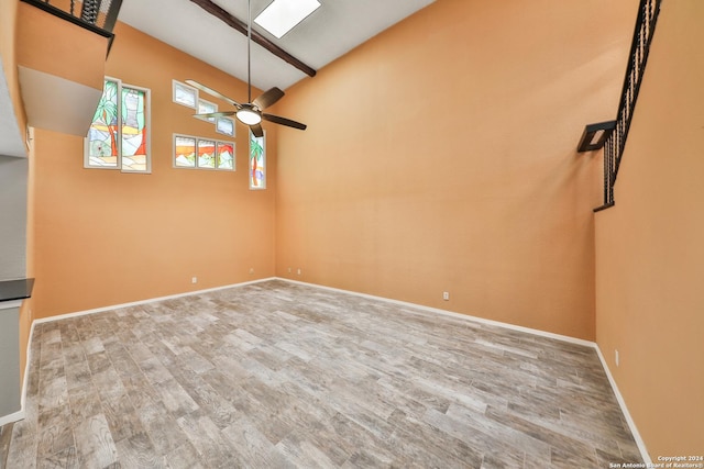 unfurnished living room with hardwood / wood-style flooring, ceiling fan, high vaulted ceiling, and beam ceiling