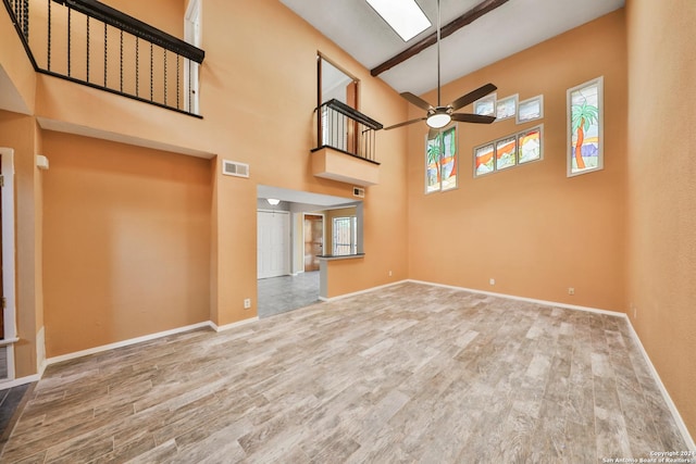 unfurnished living room featuring ceiling fan, hardwood / wood-style flooring, beamed ceiling, and a high ceiling