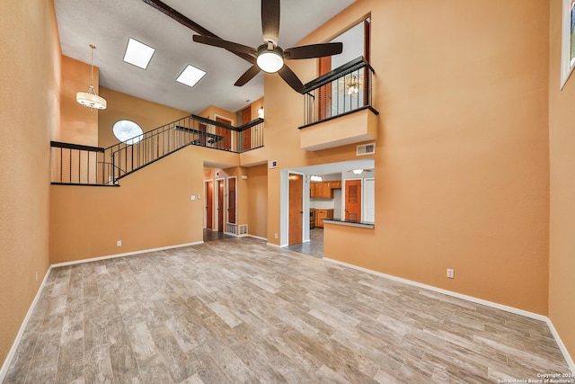 unfurnished living room featuring a towering ceiling, ceiling fan, and light wood-type flooring