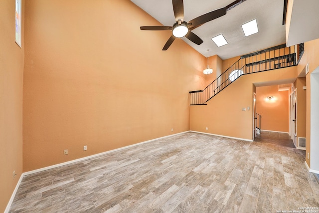 unfurnished living room featuring wood-type flooring, a towering ceiling, and ceiling fan