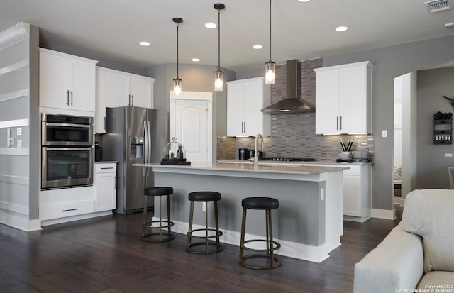 4805 Whaler, San Antonio, TX 78245 - kitchen featuring appliances with stainless steel finishes, pendant lighting, white cabinets, a kitchen island with sink, and wall chimney range hood