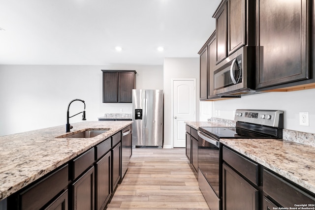 kitchen with stainless steel appliances, sink, dark brown cabinets, light hardwood / wood-style floors, and light stone countertops