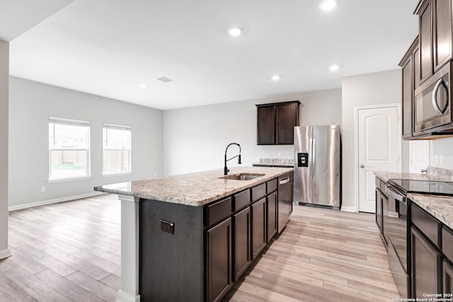 kitchen featuring light hardwood / wood-style flooring, a kitchen island with sink, stainless steel appliances, light stone countertops, and sink