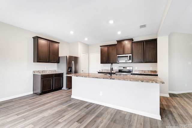 kitchen featuring light wood-type flooring, stainless steel appliances, light stone countertops, dark brown cabinetry, and sink