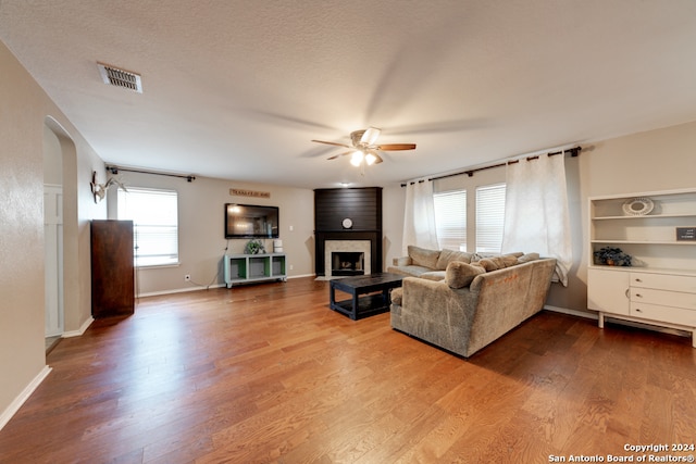 living room featuring a textured ceiling, a fireplace, ceiling fan, and hardwood / wood-style floors