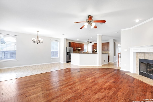 unfurnished living room featuring a tiled fireplace, a wealth of natural light, light hardwood / wood-style flooring, and ceiling fan with notable chandelier