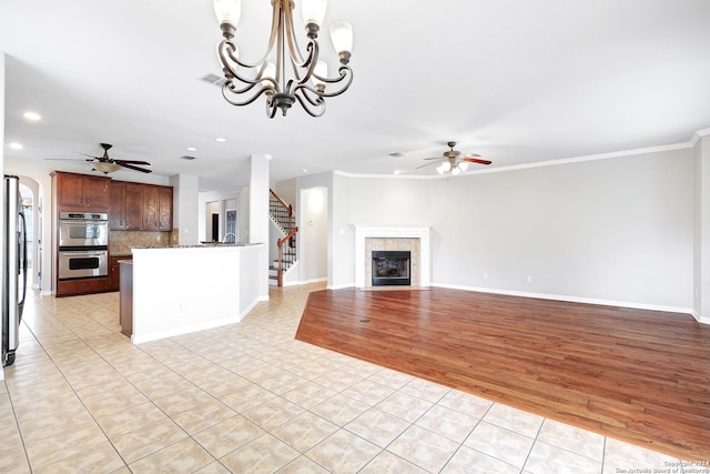 unfurnished living room with a tiled fireplace, ceiling fan, and light tile patterned flooring