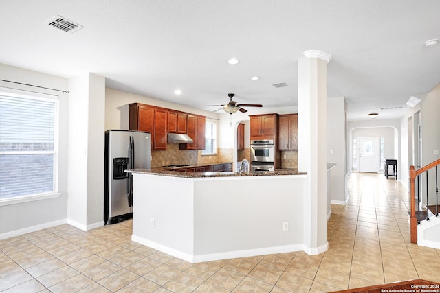 kitchen with stainless steel appliances, light tile patterned floors, decorative backsplash, and dark stone countertops